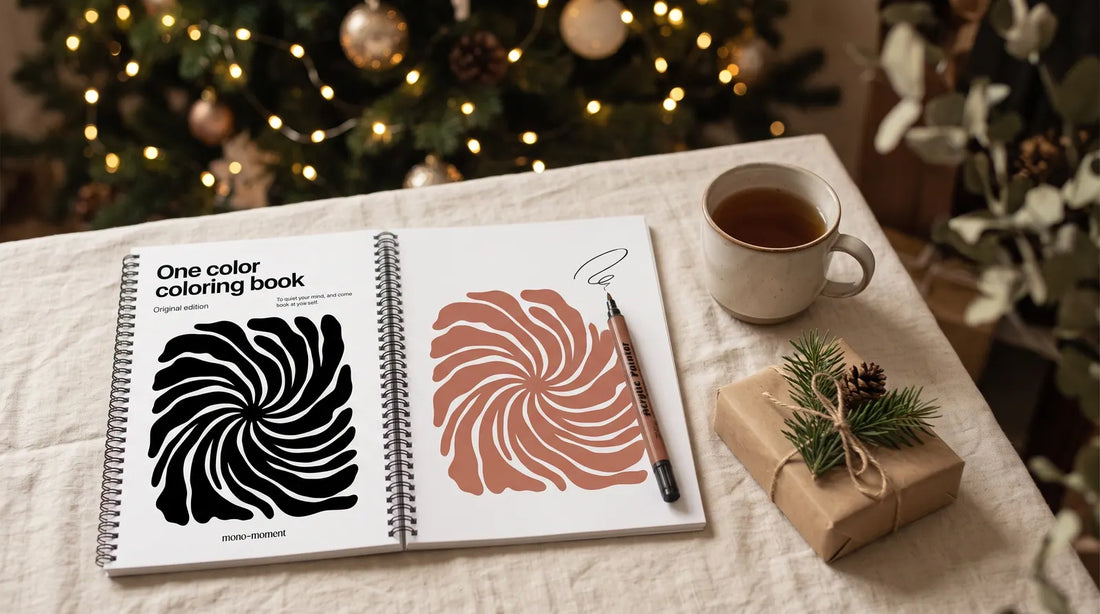 A wrapped gift, a mug of tea and an open one-color coloring book with one bold shape filled by a single pen, by a Christmas tree
