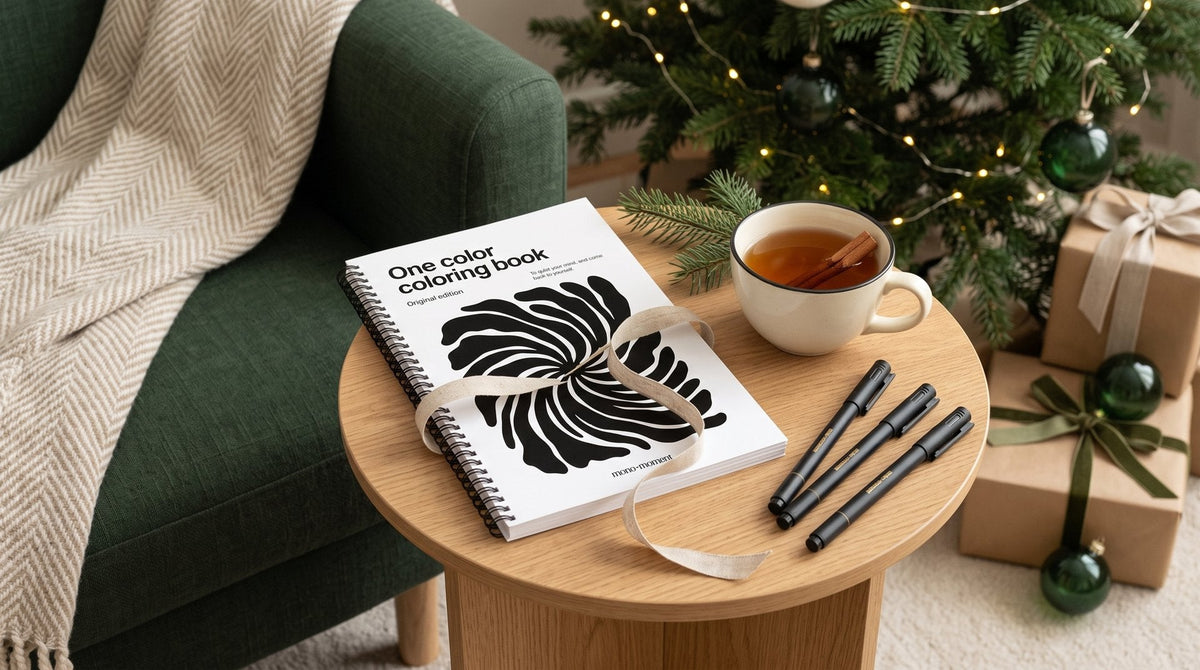 The One Color Coloring Book and three brush pens on a side table beside an armchair, with a lit Christmas tree in the background