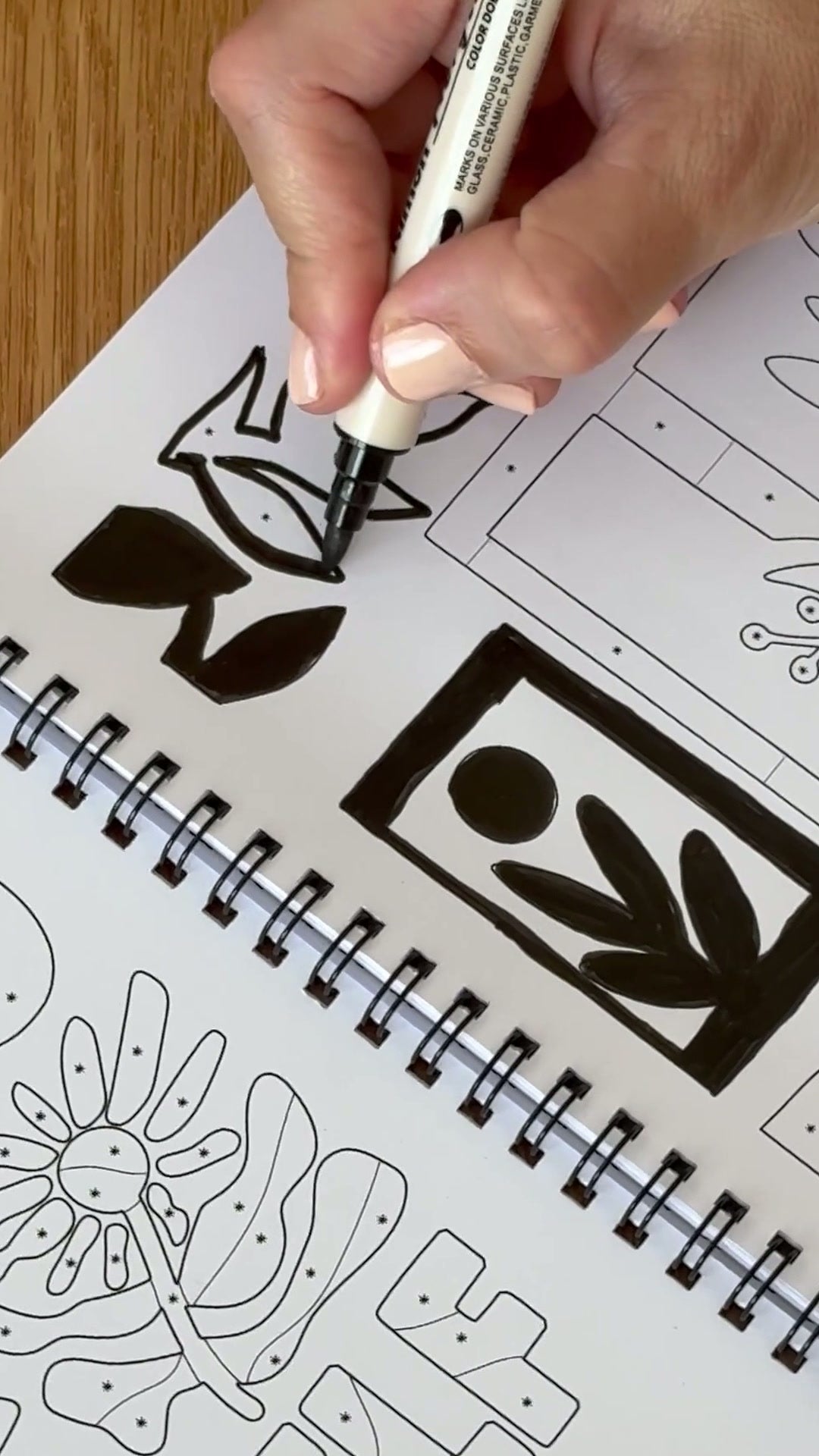 A hand filling a bold black shape with a single acrylic pen in the One Color Coloring Book