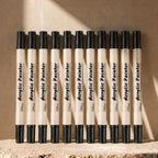 Twelve black-ink dual-tip brush pens arranged on a warm background