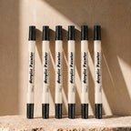 Six black-ink dual-tip brush pens arranged on a warm background